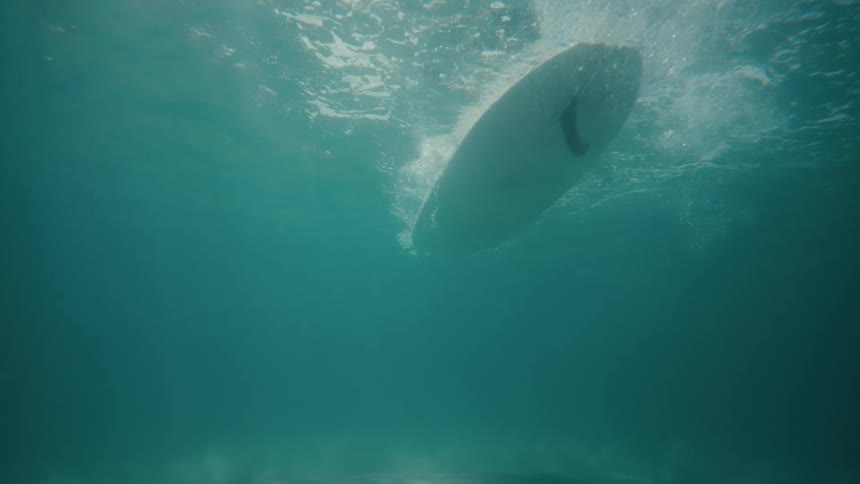 An underwater view captures the bottom of a surfboard slicing through the water