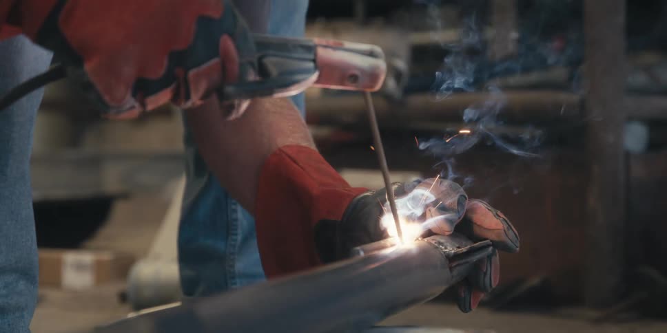 Welder wearing gloves welds a project on the floor of a workshop