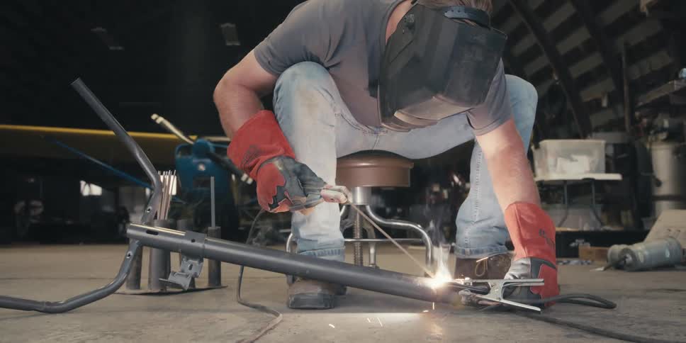 A person in protective gear is welding metal pieces together with bright sparks flying