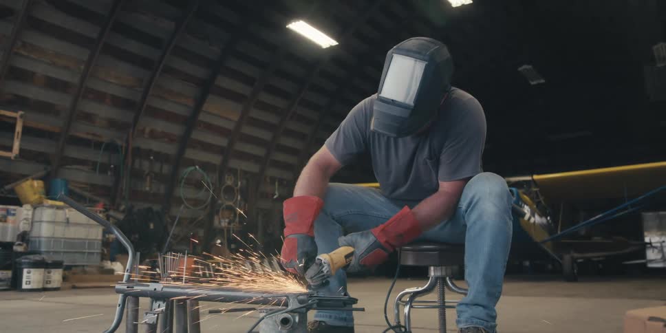 Man in helmet sitting holding a tool and welding a metal