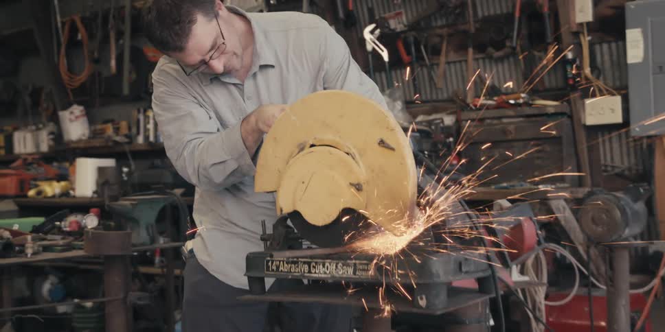 A man is working on a machine that is emitting sparks in a room with numerous tools all over