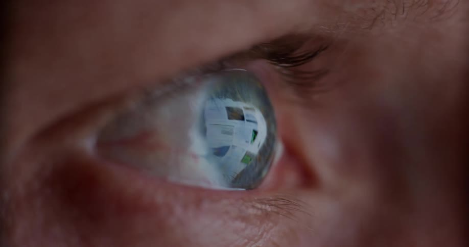 A persons eye with a blue iris and a reflection of a screen passing over their eye