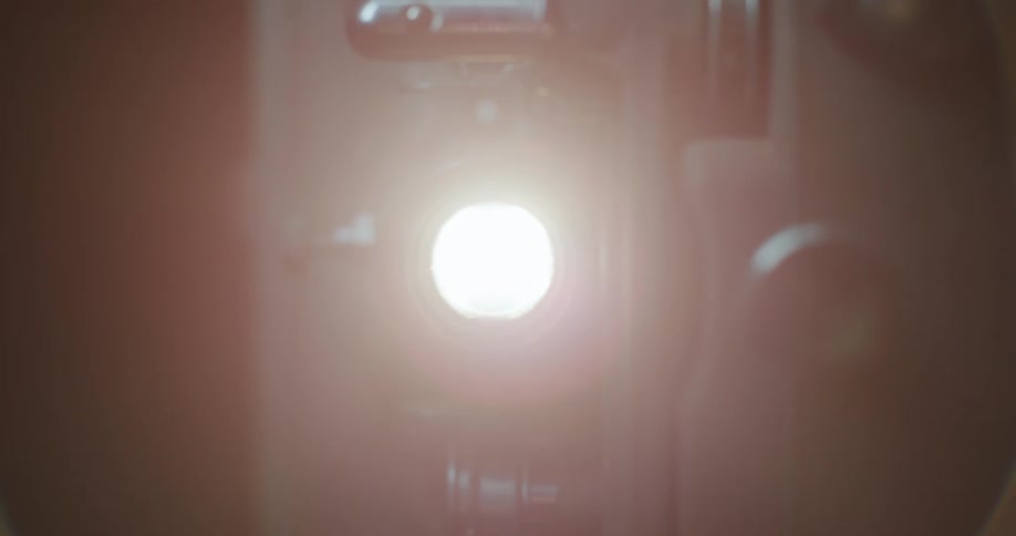 A closeup of an old film projector with its lens glowing brightly