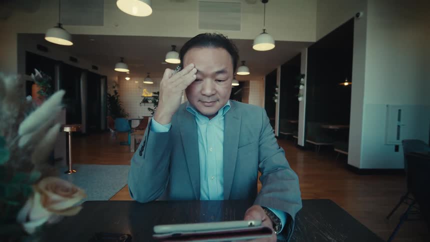 A man sitting in front of a black table and holding a book and then starts talking on his cell phone
