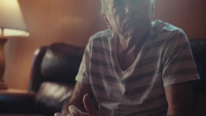 Elderly man with hands clasped sitting on the sofa in the living room