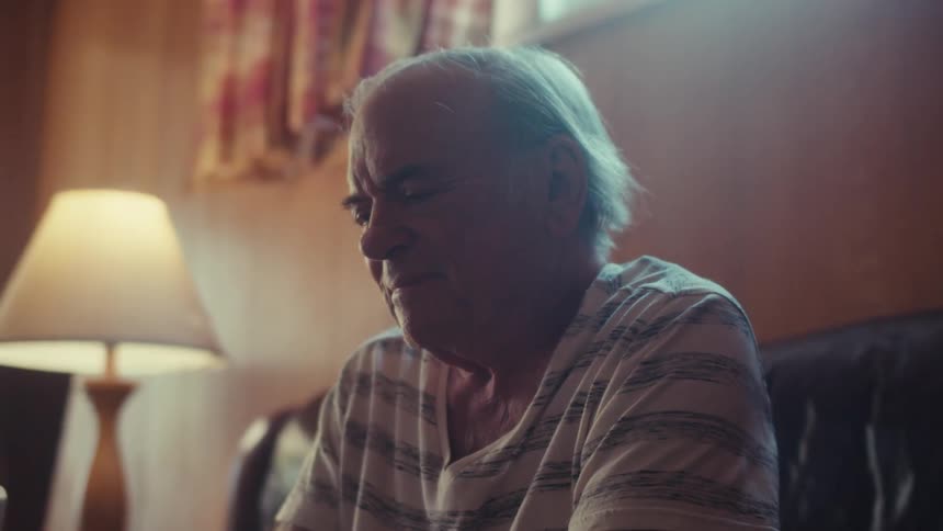 An elderly man sits on the couch happily viewing something on his tablet