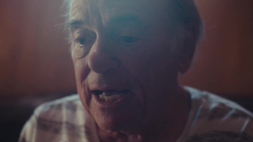 A happy elderly person with white hair is laughing indoors wearing a striped shirt with soft lighting illuminating the scene