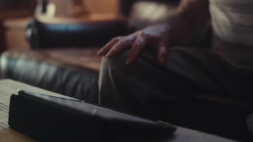 Aged hand delicately touches the screen of a tablet resting on a wooden surface