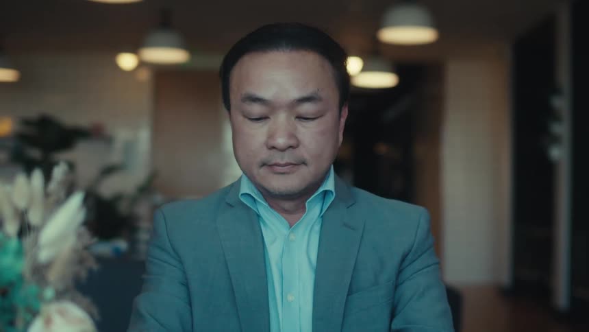 A man in a suit uses a tablet puts a pen to his chin answers his phone and returns to using the tablet