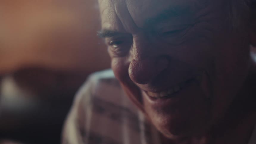 The face of an elderly man who is smiling while looking forward and shaking his head