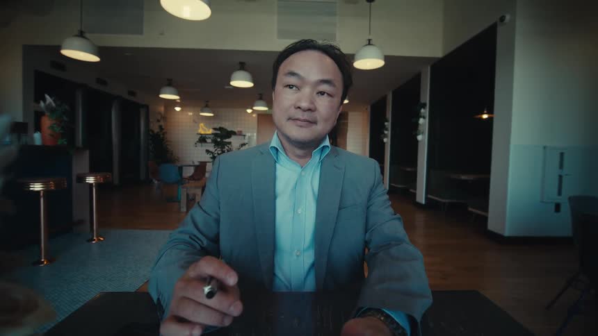 A businessman in a suit uses a tablet smiling in a room with ceiling lamps in the background