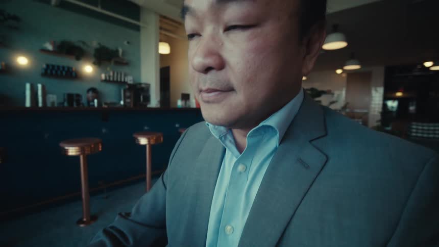 A man is typing on his tablet as he sits at a table in a bar