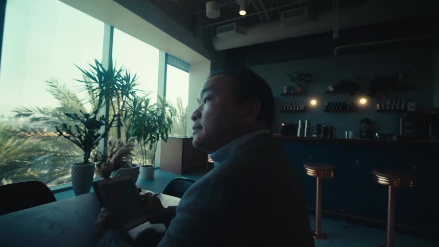A person sits alone at a table in a modern welllit caf with large windows showing palm trees and a cityscape in the background