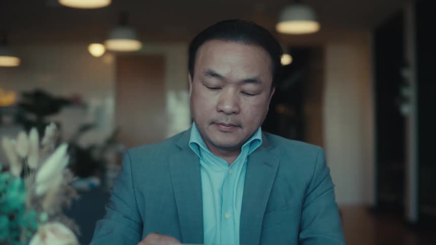 A person in a suit is sitting at a table in a modern stylish caf with a tablet answering a call on his phone
