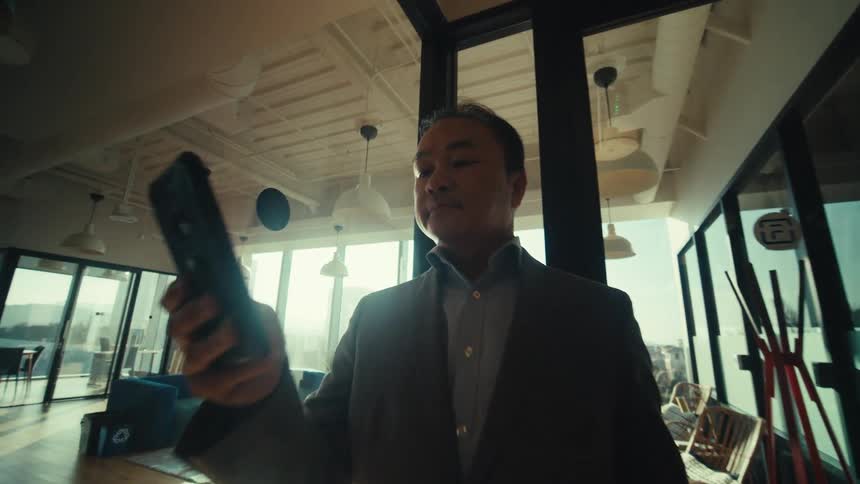 A person in a suit is standing on a modern office hallway while looking at a smartphone