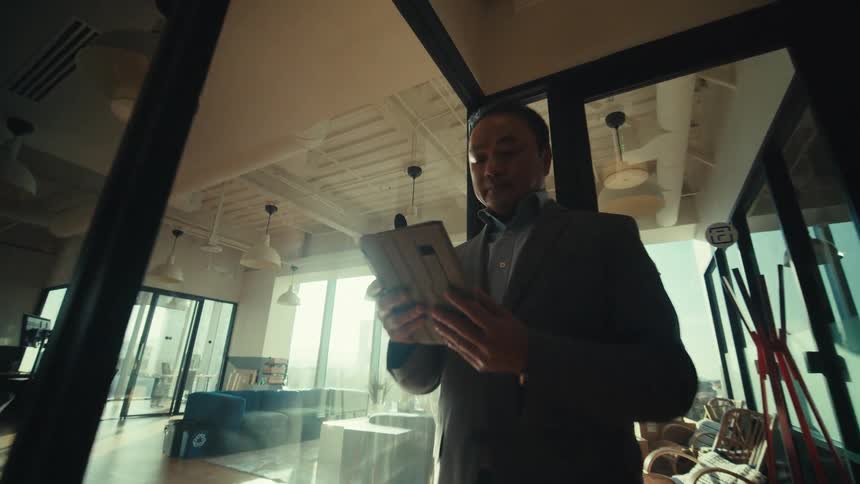 A person in a suit is walking down a modern office hallway while looking at a tablet
