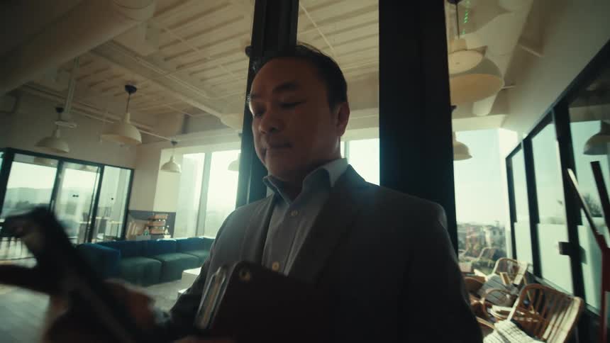 A man holding a tablet stands in a room full of large windows