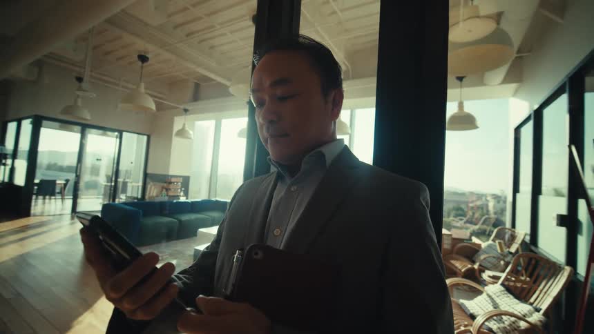 A person in a suit is standing on a modern office hallway while looking at a smartphone