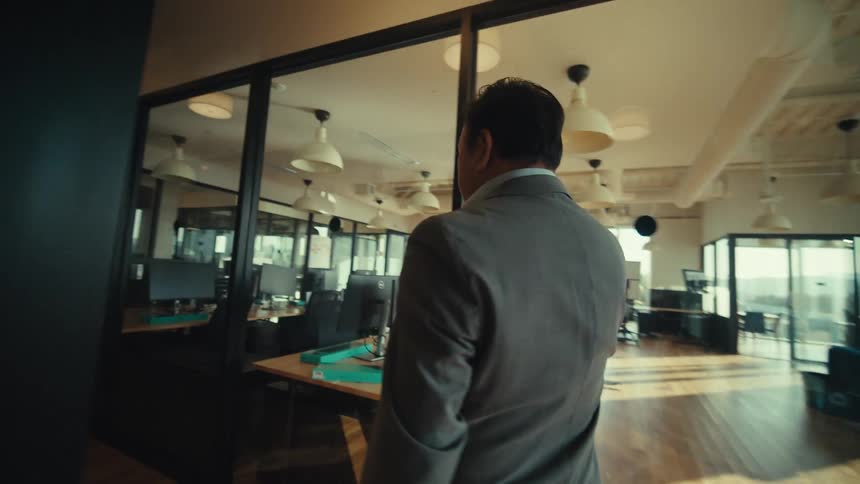 A person in a suit is walking down a modern office hallway while talking on a smartphone