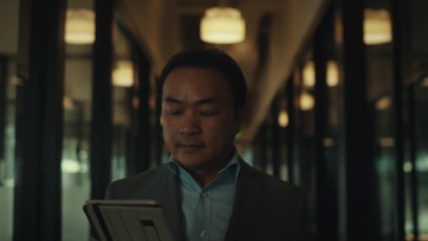 A person in a suit is walking down a modern office hallway while looking at a tablet