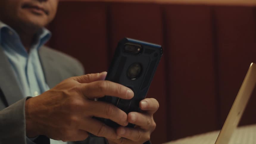 Man in a suit sitting typing on an iphone with a laptop in front of him open