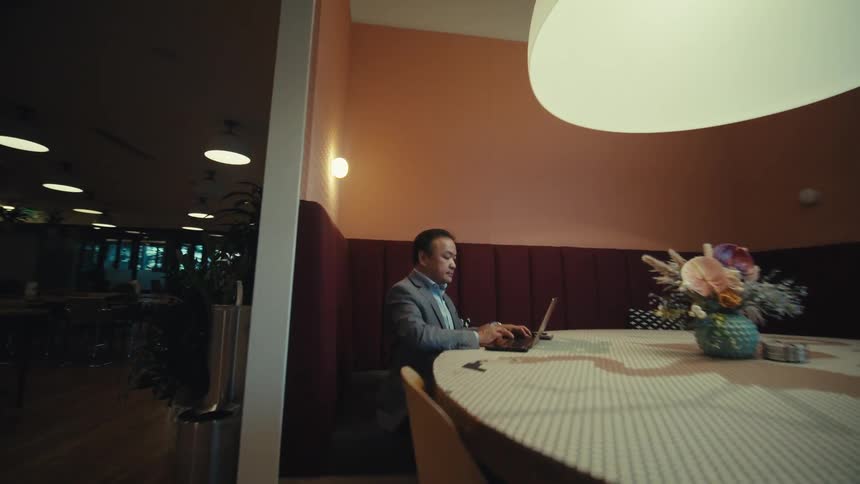A person is sitting at a large round table in a modern warmly lit dining area with wooden floors