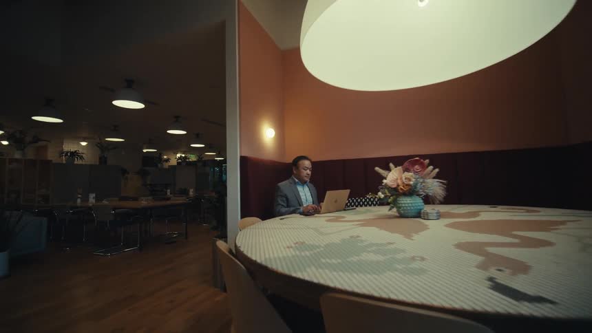 A person is sitting at a large round table in a modern warmly lit dining area with wooden floors