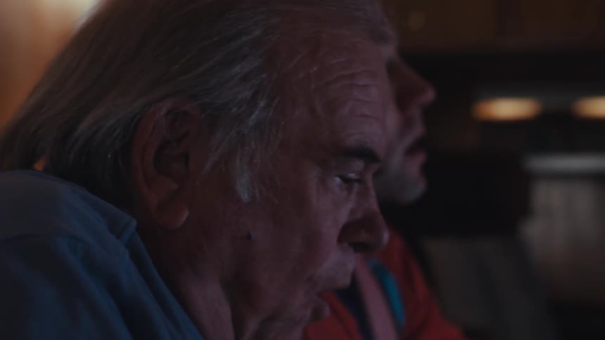A young man next to an elderly man who are sitting nervously as they look and talk ahead