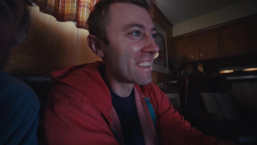 An older man and a younger man are sitting on a couch playing a video game and the younger man becomes very animated as they play