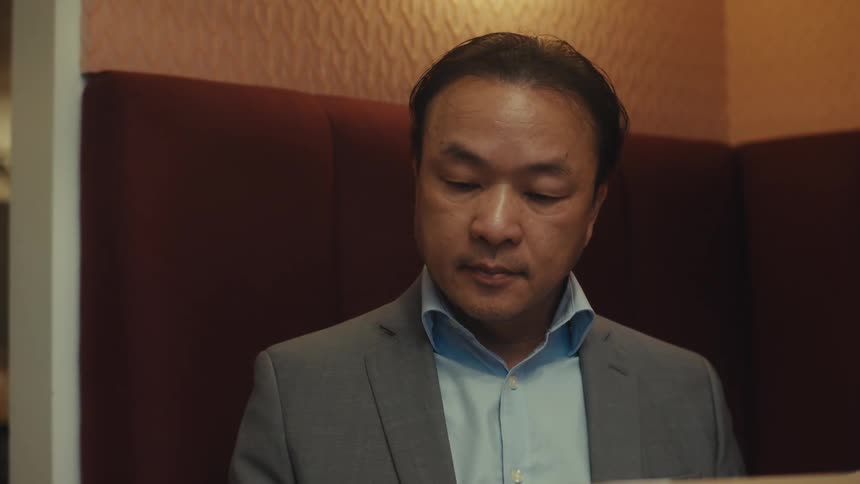 A person in a suit sitting at a table working on a laptop and looking at a smartphone