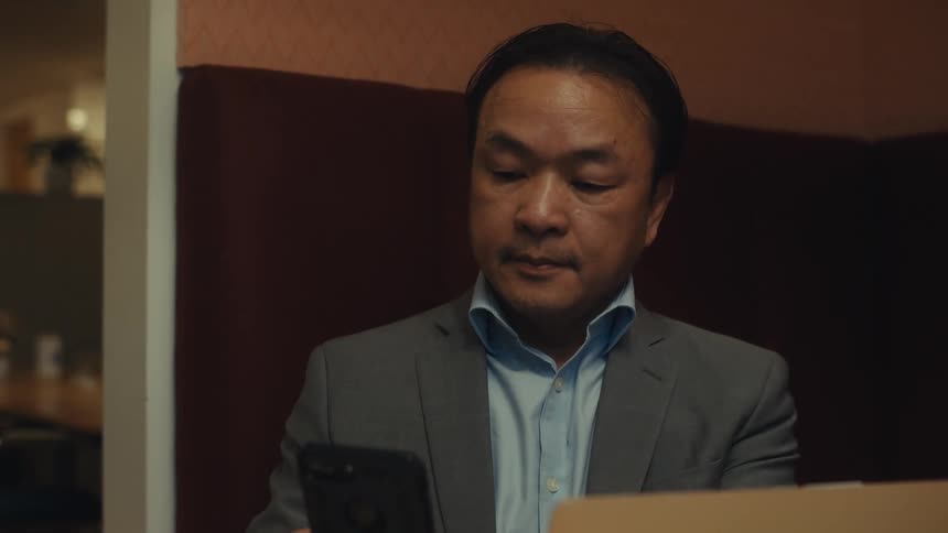 A person in a gray suit is sitting in a booth working on a laptop in a dimly lit room