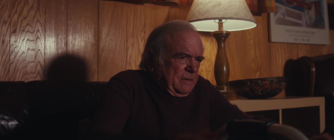 A man sitting down in a dimly lit room his hands resting on the handles of a walker