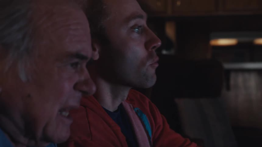 Younger man shows elderly man how to play a console game at home