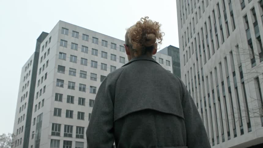 A woman wearing a coat walking near modern buildings in a city at fall