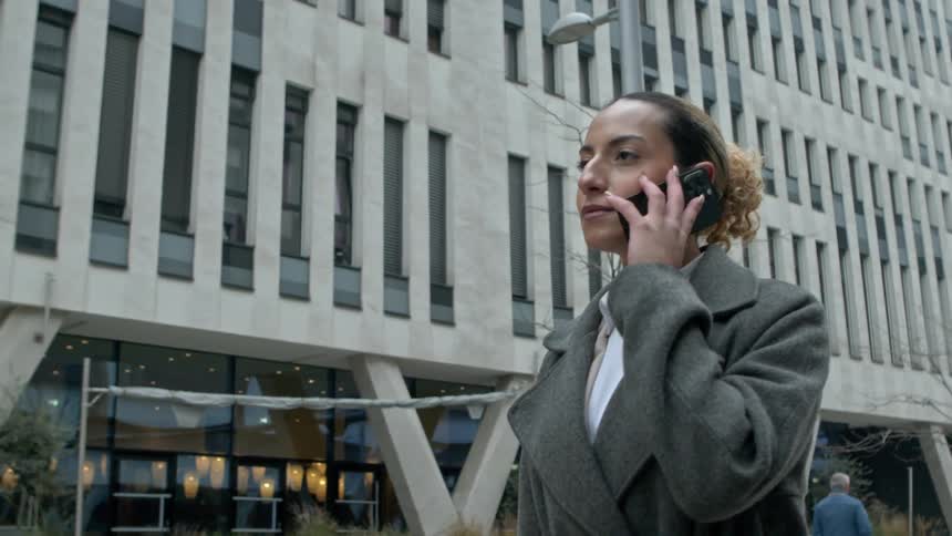 A woman answers her phone while walking in the city
