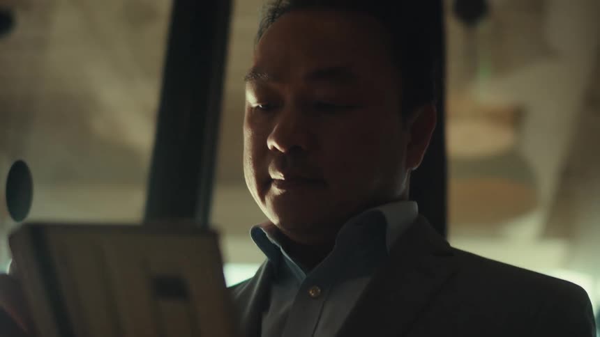 A person in a suit is holding and looking at a tablet in a modern welllit office