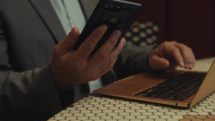A man working on a laptop picks up a smartphone from the table
