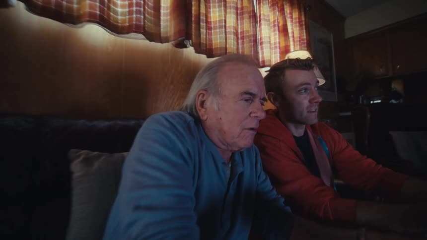A father and son are playing a video game together on a sofa in a living room