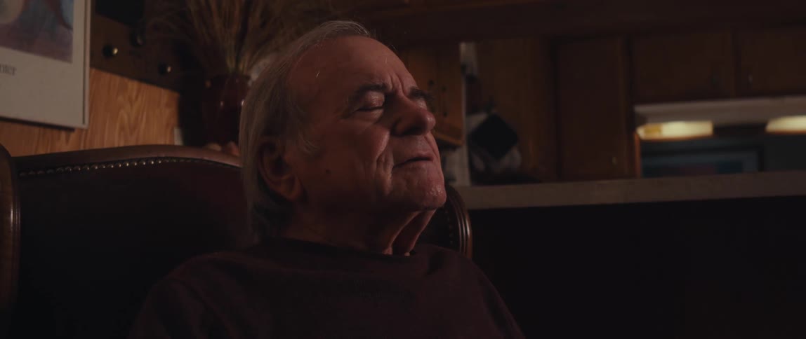 An elderly man sits down in a comfortable chair at home and relaxes