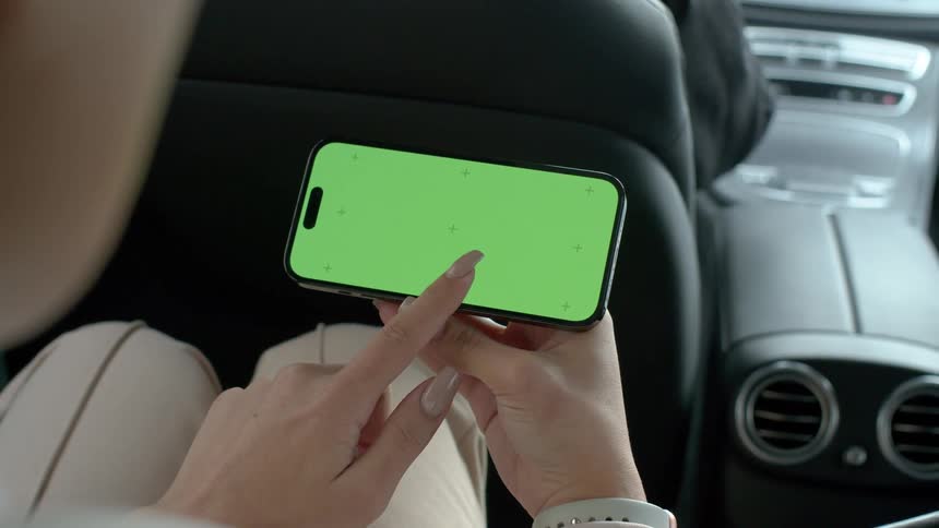 A person inside a car moving his finger on a cell phone screen with a green screen