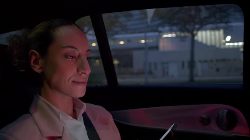 Elegantly dressed woman sitting in the back seat of a car at dusk using her cell phone