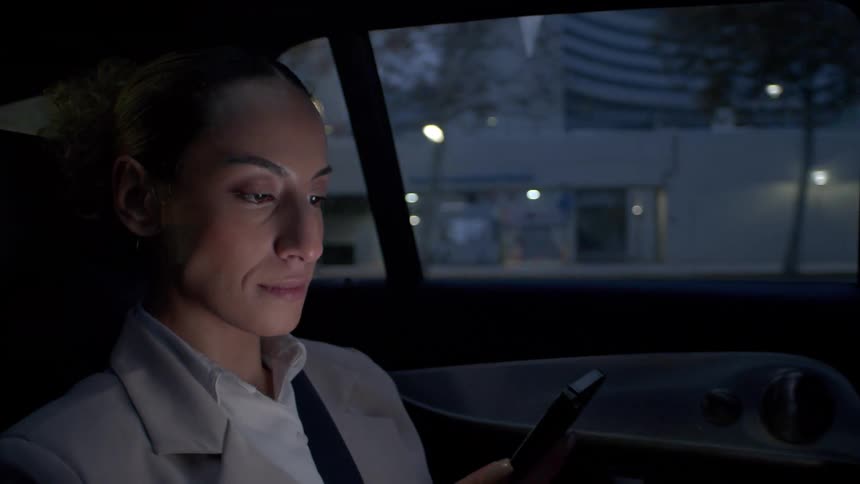 A woman is using her phone as she rides in the car