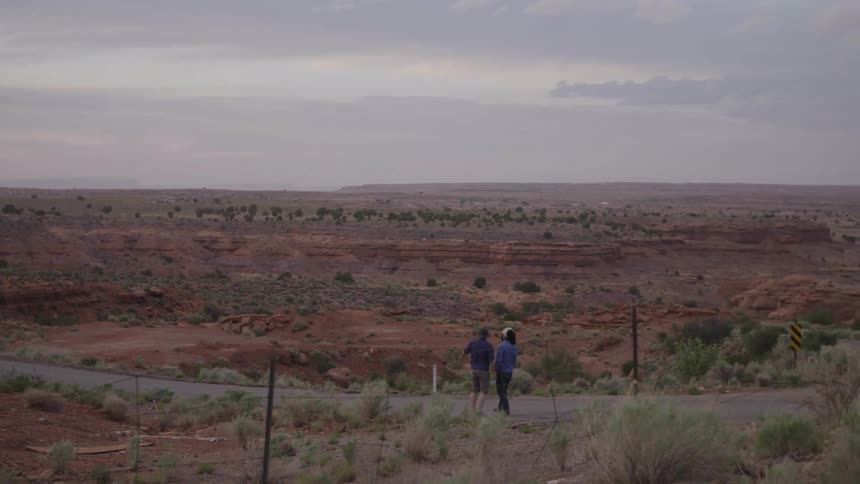A man and a woman standing on the side of the road in an otherwise empty desert