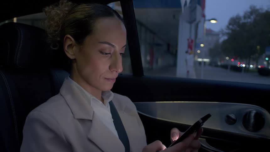 Female passenger riding in a ride share car at night texting on cell phone