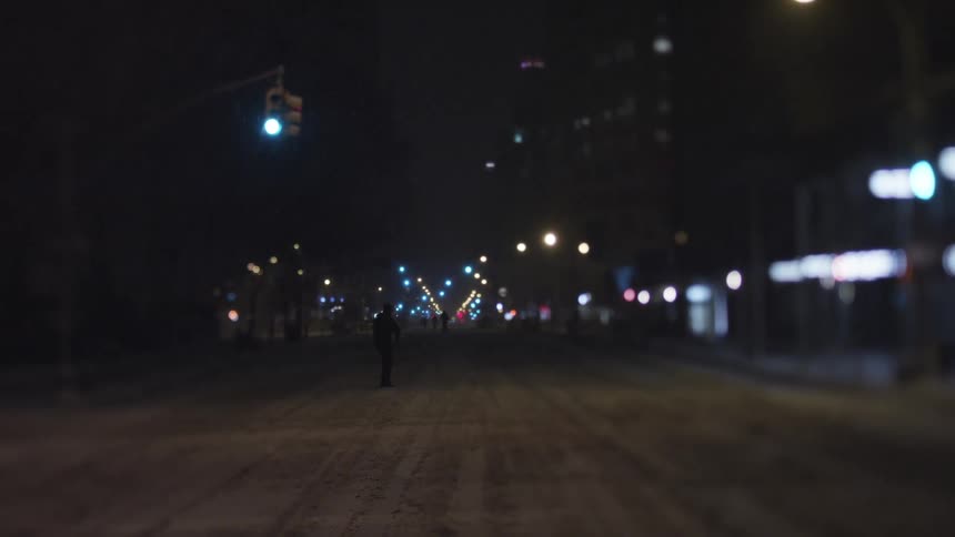 Large road with a man walking down and many street lights at night