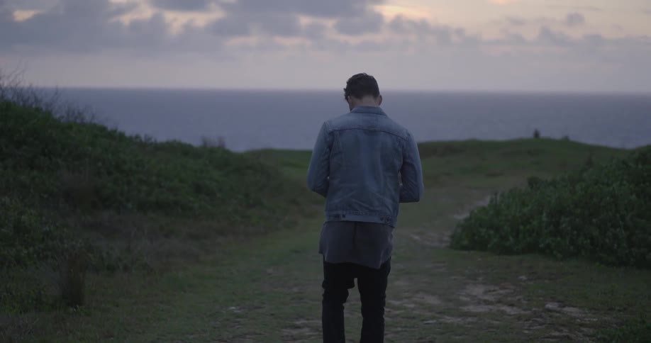 A man in a denim jacket walks towards the ocean