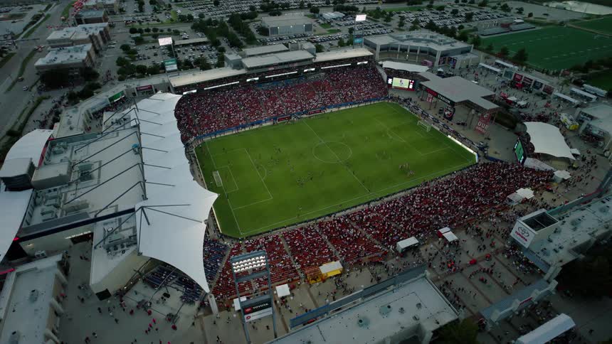An aerial view of a packed soccer stadium during a match with a large crowd filling the stands