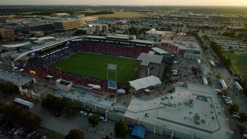 A bustling stadium surrounded by city buildings and parking lots filled with fans for a game