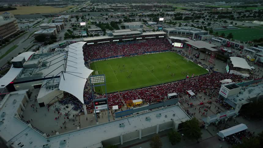 An aerial view of a soccer stadium with green grass and stands full of people