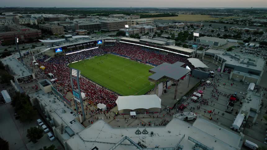 Aerial view captures toyota stadium at dusk showcasing a packed crowd enjoying a soccer match under the glow of stadium lights against a backdrop of the surrounding cityscape